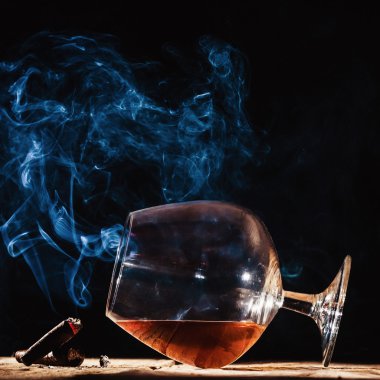 Glass of alcohol and smoking noble cigar on a black background clipart