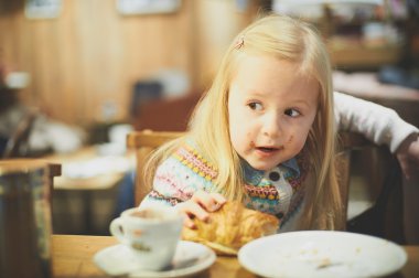 Küçük sarışın kız sıcak süt içme bir kafede