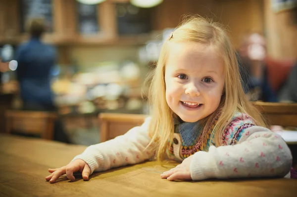 Niña rubia en un café bebiendo leche caliente — Foto de Stock