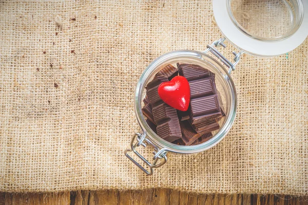 Chocolate y corazón en un frasco sobre un fondo de madera en el día o — Foto de Stock