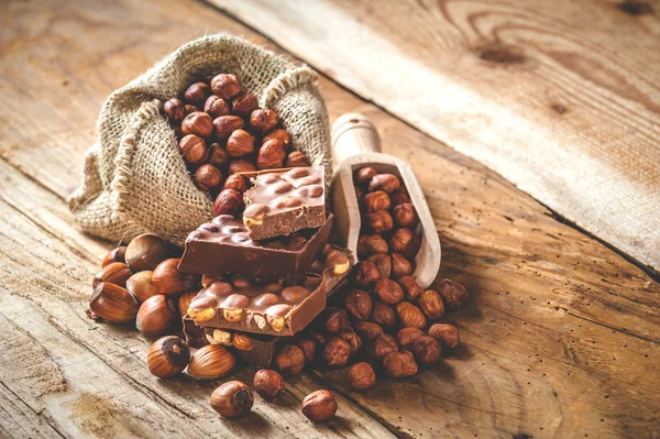 Melkchocolade met hazelnoten en walnoten in een zak op een houten — Stockfoto