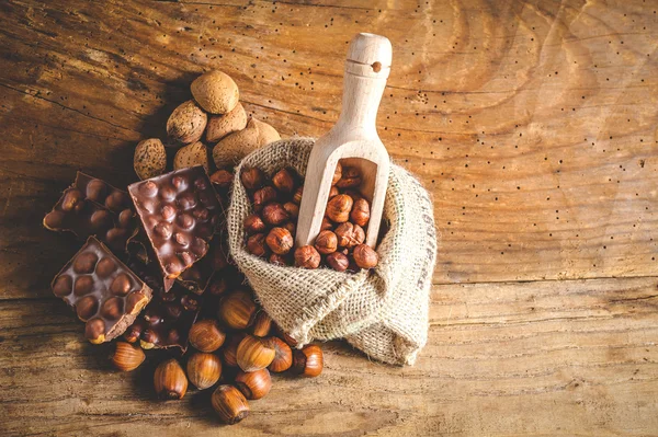 Melkchocolade met hazelnoten en walnoten in een zak op een houten — Stockfoto