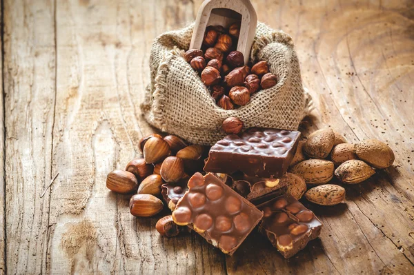 Melkchocolade met hazelnoten en walnoten in een zak op een houten — Stockfoto