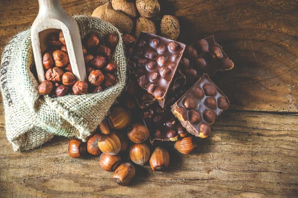 Melkchocolade met hazelnoten en walnoten in een zak op een houten — Stockfoto