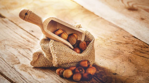 Hazelnoten in een landelijke zak op een houten tafel en een lepel voor scoop — Stockfoto