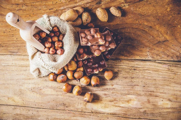Cioccolato al latte con nocciole e noci in un sacco su un legno — Foto Stock