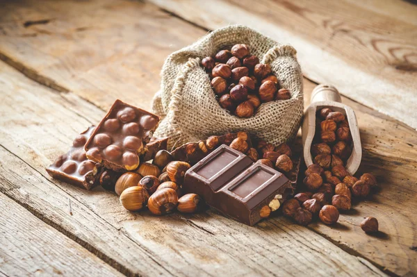 Milk chocolate with hazelnuts and walnuts in a sack on a wooden — Stock Photo, Image