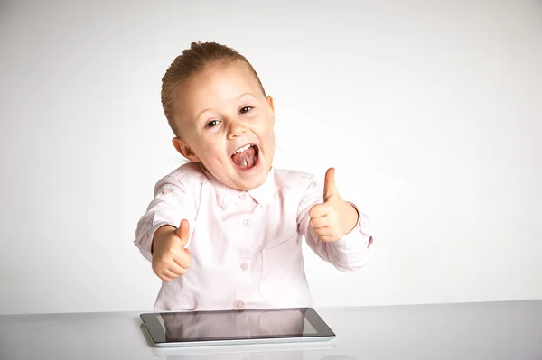 Linda niña pequeña y sonriente juega con una tableta — Foto de Stock