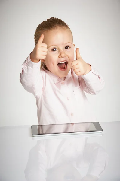 Linda niña pequeña y sonriente juega con una tableta — Foto de Stock