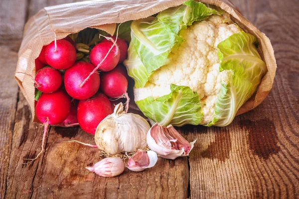 Radieschen und Blumenkohl in einer Papiertüte auf einem Holztisch — Stockfoto