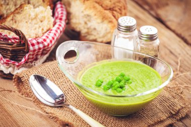 Rustic green pea soup in a transparent bowl with bread.