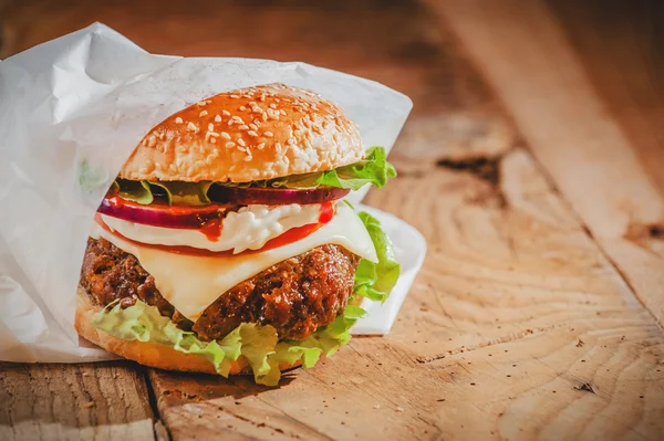 Chutný hamburger s rychlým občerstvením v bílé knize o dřevěným ta — Stock fotografie