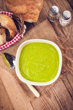 Green pea soup in a bowl with bread and sour cream on rustic lin