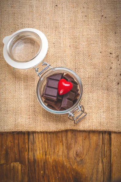 Chocolate y corazón en un frasco sobre un fondo de madera en el día o — Foto de Stock