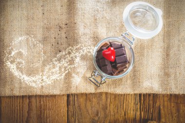 Chocolate and heart in a jar on a wooden background on the day o clipart