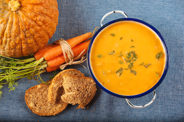 Soup with pumpkin and carrot on a blue tablecloth in country sty