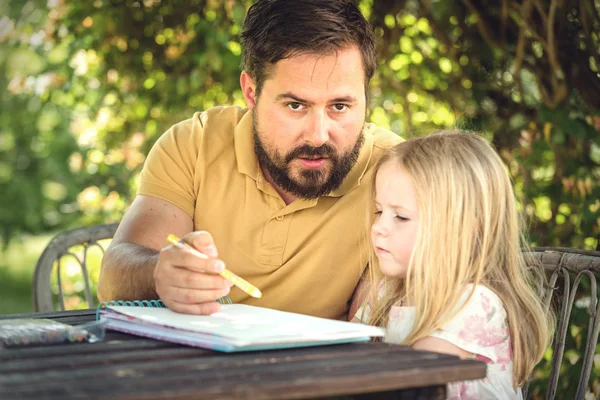 Padre con hija en el jardín en la mesa, haciendo deberes. Fotos De Stock