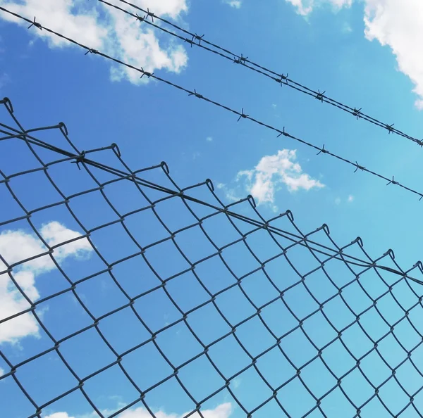 Колючий дріт паркан з білими хмарами і синім фоном неба — стокове фото