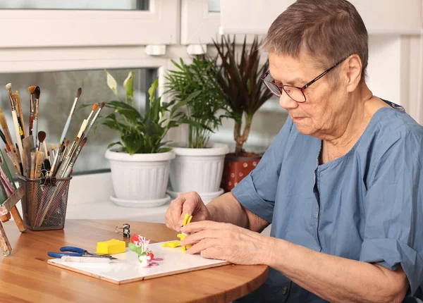 Aktif yaşlılık. Yaşlı bir kadın, polimer kilden küçük oyuncaklar yontuyor. Sanat terapisi. 80 yaşındalar. Mutlu, yaşlı bir insan yaratıcılıkla meşgul olur.