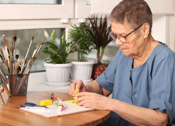 Una vejez activa. Una anciana esculpe pequeños juguetes de arcilla polimérica. Terapia artística. la edad de 80 años. Un anciano feliz se dedica a la creatividad —  Fotos de Stock