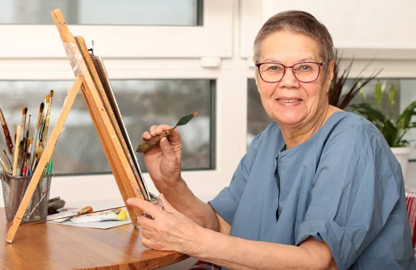 Літня жінка малює фотографії вдома. вік 80 років. Щаслива літня людина займається творчістю . — стокове фото