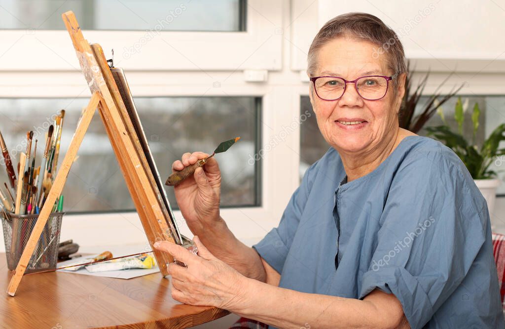 An elderly woman draws pictures at home. the age of 80 years. Happy elderly person is engaged in creativity.