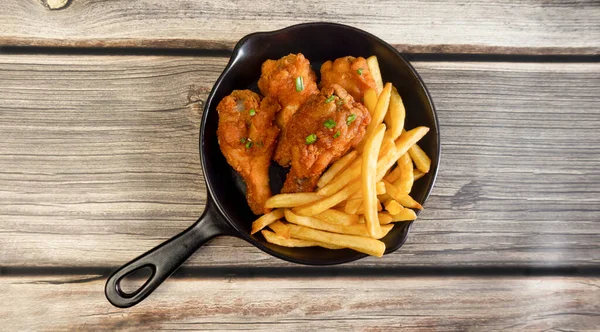 Küçük siyah tavada kızarmış tavuk ve patates kızartması..