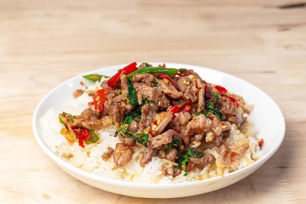 Biftek ve kutsal fesleğenle kaplanmış pirinci ahşap masaya koy. Popüler Tayland sokak yemekleri..