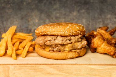 Çedar peynirli duble burger sebze yok, patates kızartması ve ahşap tabakta kızarmış tavuk..