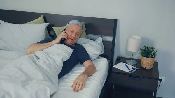 A man wakes up in bed and talks sleepily on the phone.