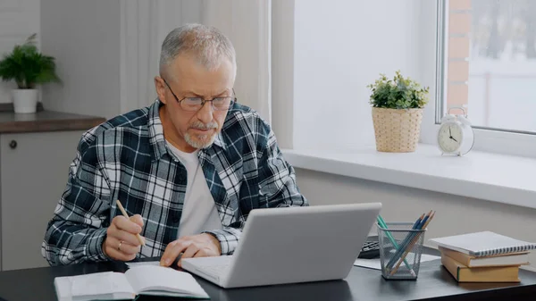 An elderly man keeps financial records at a computer.