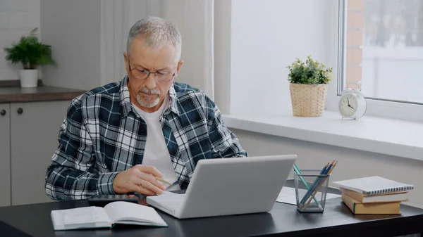 An elderly man keeps financial records at a computer.