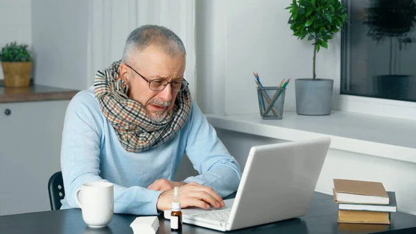 A sick elderly person sits at a laptop and suffers from the flu and a high fever.