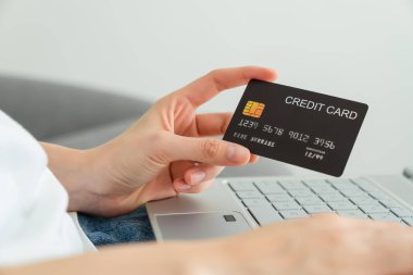 Kredi kartı tutan eller ve internetten alışveriş yapan dizüstü bilgisayarlar..