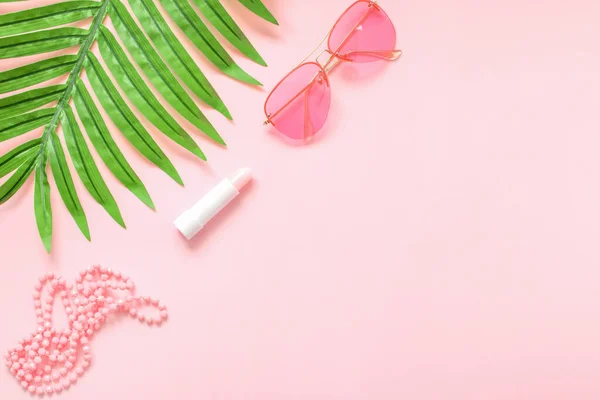 Women\'s fashion accessories and cosmetics of pink color isolated on pink background with palm leaf. Pink glasses. Magazines, social networks. View from above. Flat lay.