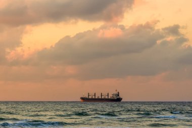 Günbatımında (gündoğumunda) denizde kargo gemisi. Deniz manzarası ve renkli bulutlar. 