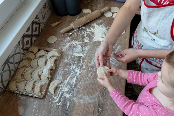 Мама учит своего маленького кавказского ребенка готовить вареники. — стоковое фото
