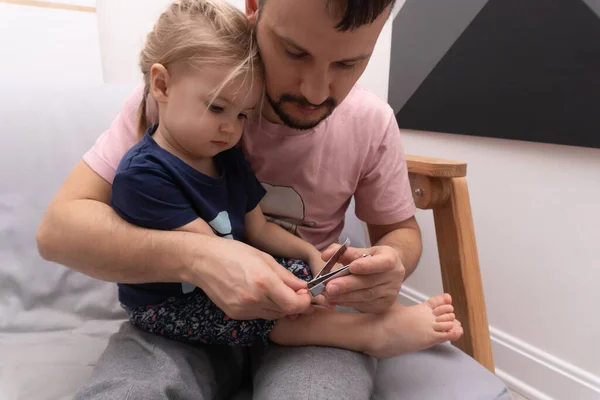 Καυκάσιος μπαμπάς κόβει τα νύχια προσεκτικά με κλαδευτή στο χαριτωμένο καυκάσιο παιδί του Royalty Free Εικόνες Αρχείου