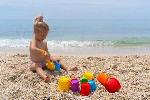 Lindo niño caucásico juega con juguetes coloridos en la orilla del mar de arena. — Foto de Stock