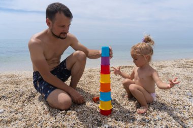 Young dad plays with daughter making colourful pyramid