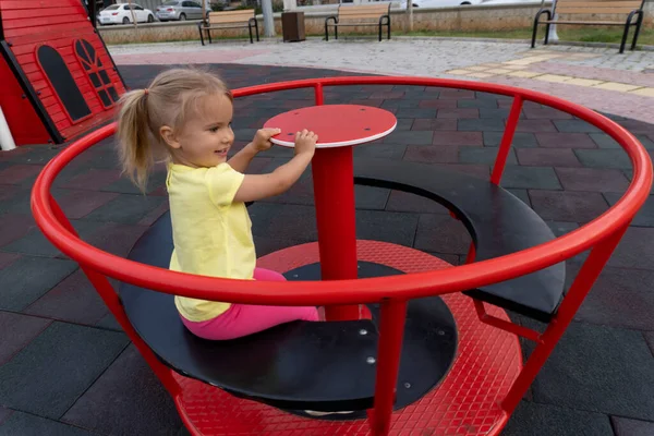 Cute little caucasian child riding on spining swing at playground — Φωτογραφία Αρχείου