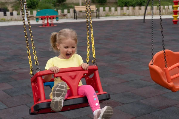 Cute caucasian child swings on swing, laughing and crying with happy expression — Φωτογραφία Αρχείου