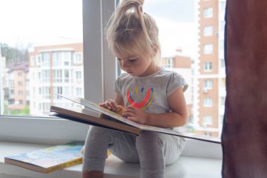 Sevimli beyaz çocuk pencerenin yanına oturur ve kitap okur..