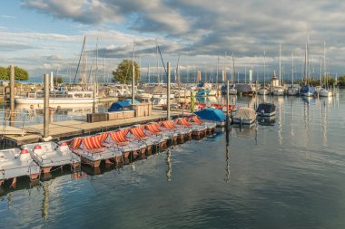 Romanshorn Limanı, Constance Gölü, Thurgau Kantonu, İsviçre. Pedal tekneleri, motorbotlar ve yelkenliler parçalı bulutlu bir gökyüzünün altında demirli.