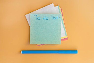 Yapılacaklar listesi olan kare not kağıdı. Sarı arka planda çok renkli notlar ve mavi bir keçeli kalem. en üstteki görünüm.