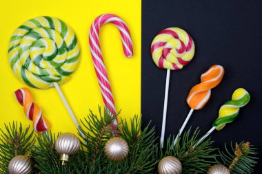 Çubukta şeker ve Noel ağacı dalları. Siyah-sarı arka plan görünümlü çok renkli şekerler. Noel tatlıları çubukta. yeni yıl kompozisyonu 