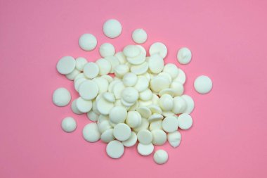 Pembe arka planda beyaz çikolata damlaları. Krema yapmak için beyaz çikolata damlası. Şekerlemeciler için beyaz çikolata..