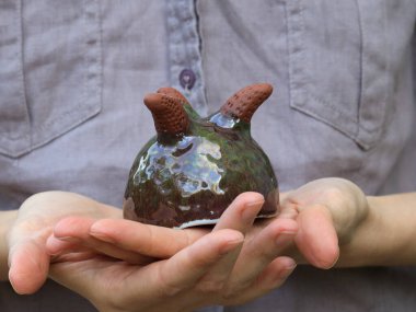 Parlak yeşil jöleli küçük el yapımı seramik ekici ve insan elinde tutulan kısa kilden bacaklar. Dokulu yüzeyi ve el yapımı formu doğal ışıkla gösteren yakın plan fotoğraf..