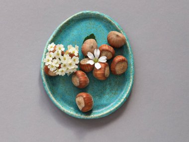 El yapımı oval seramik plaka turkuaz jöleli orman fındıkları ve gri arka planda beyaz çiçekler, iç dekorasyon için doğal sade yaşam bileşimi, yavaş yaşam.