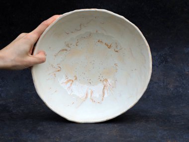 El yapımı bir seramik kasenin yukarıdan görünüşü, iç yüzeyin yumuşak beyaz bir cila ile kaplandığını gösteriyor. İnce kahverengi ve kumlu ateşleme izleri organik şekiller oluşturur, iç kısımda akış şekilleri, jölenin doğal hareketini vurgular.